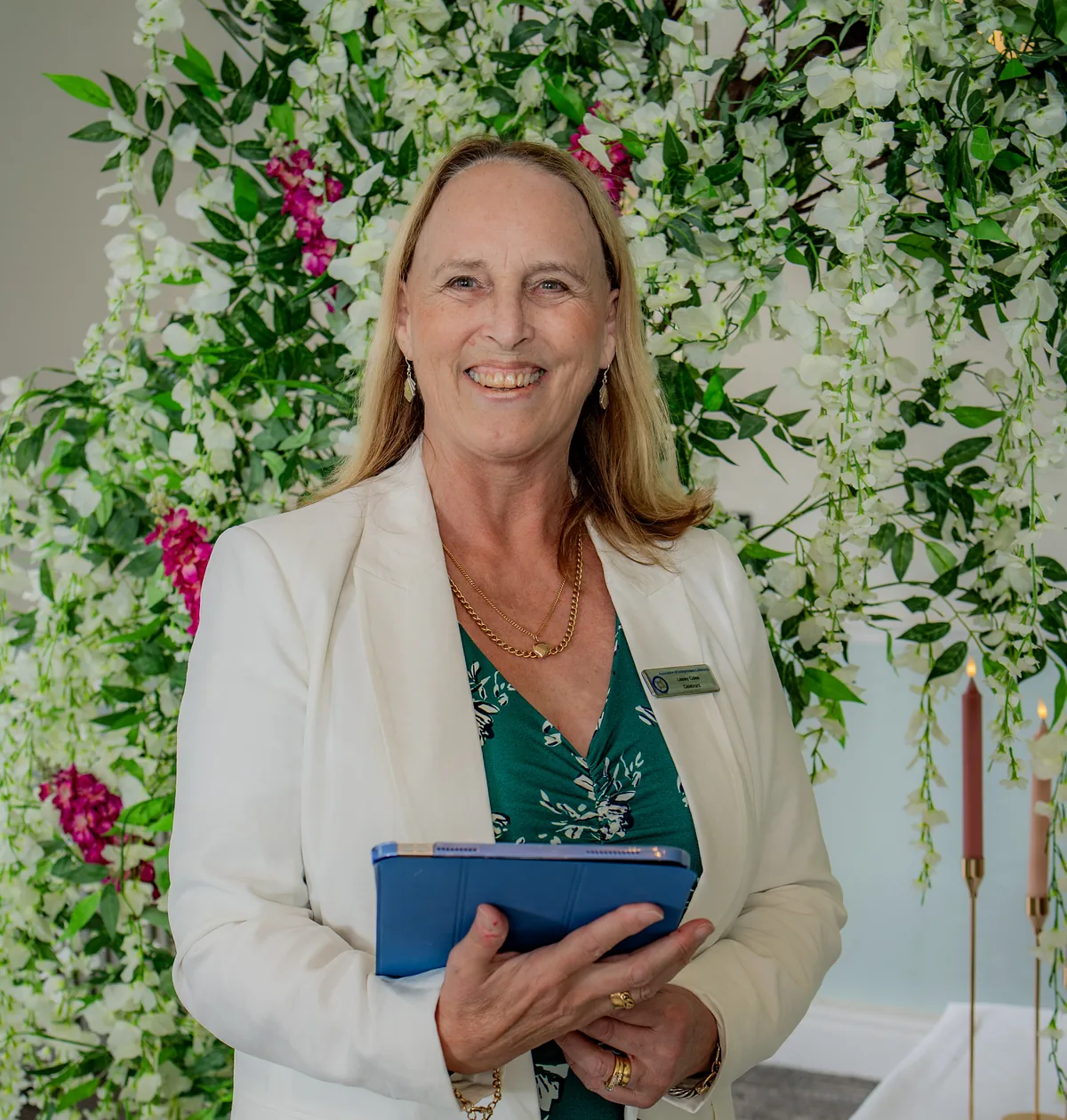 Lesley Coles, vow renewal celebrant, in front of a flower wall
