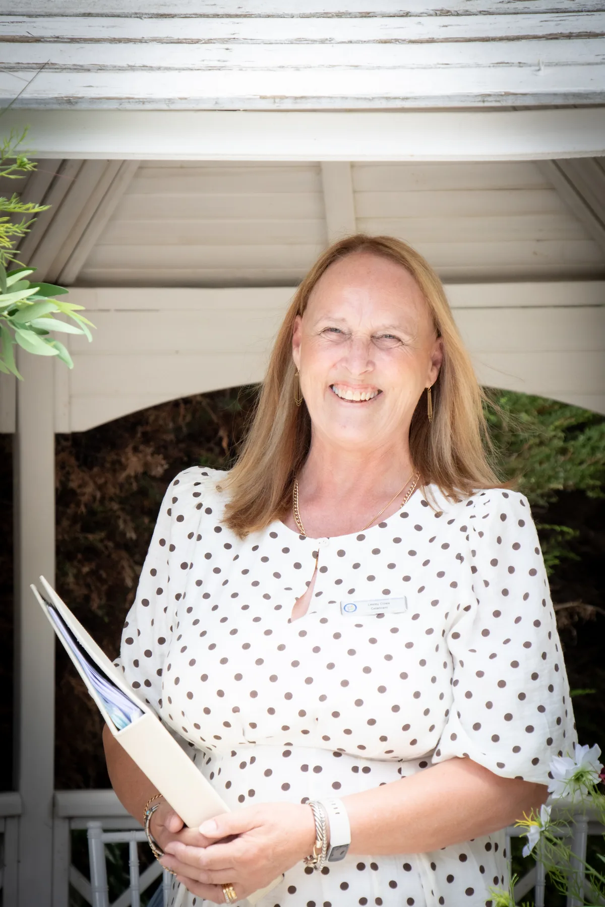 Lesley Coles, wedding celebrant, smiling and holding her ceremony folder